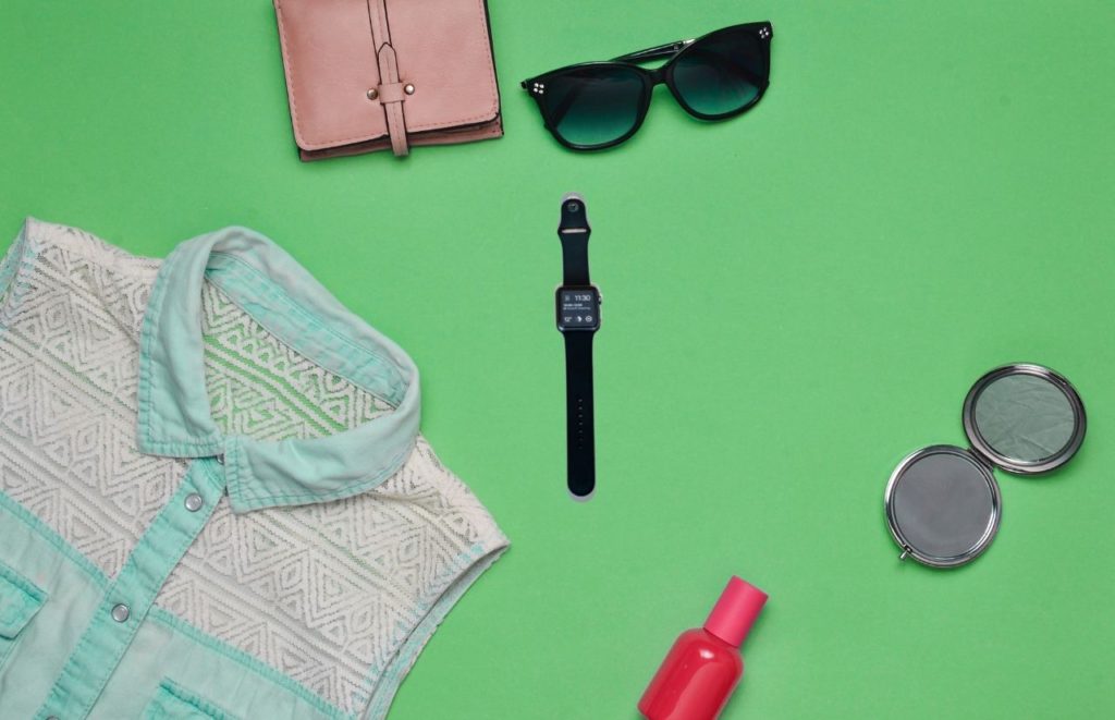 Sunglasses white shirt brown journal and black apple watch on green background. Keep reading to get the best watch travel cases and boxes.