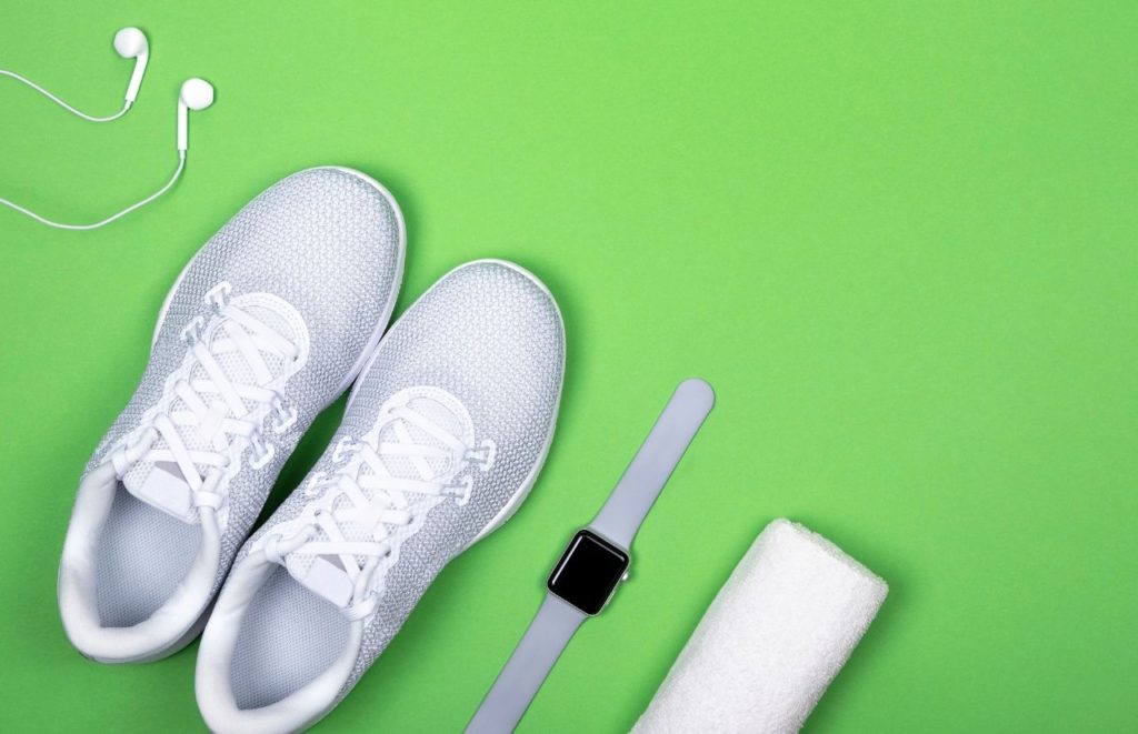 White sneakers with apple watch white towel and headphones on green background Canva. Keep reading for your full guide for your Florida beach packing list.