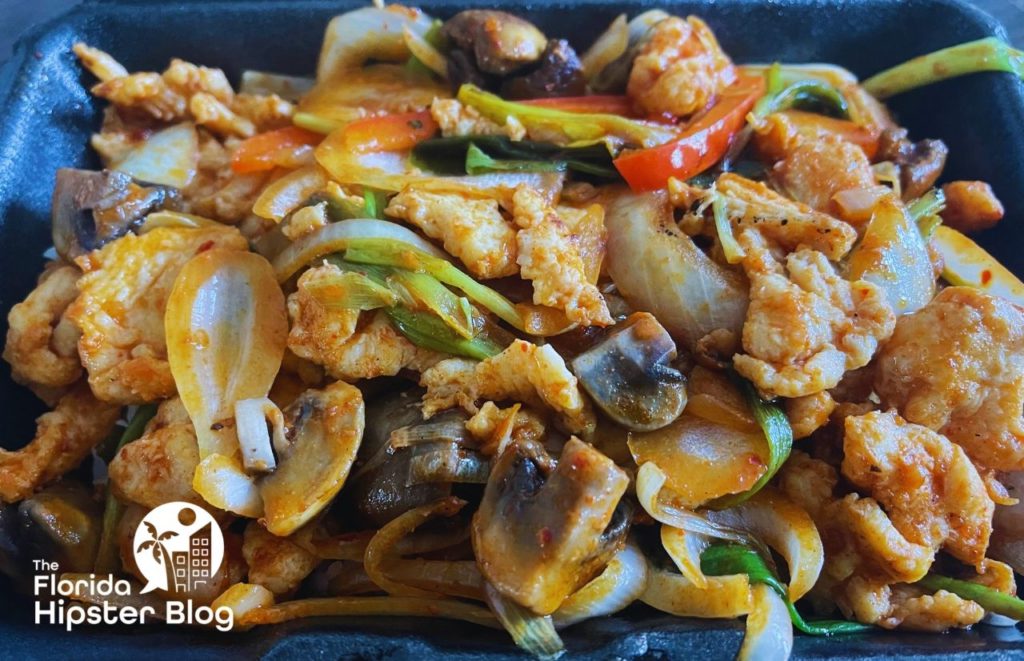 Bento Korean Asian Chicken Dish in Orlando Florida. Close-up view of chicken, mushrooms, onions, peppers and other vegetables tossed in a sauce. Keep reading to see what are the best places to get lunch in Orlando.