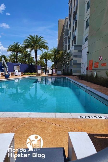 Gainesville Hotel Indigo outdoor pool area with tall palms and sun loungers. Keep reading to find out more about Hotel Indigo Gainesville.