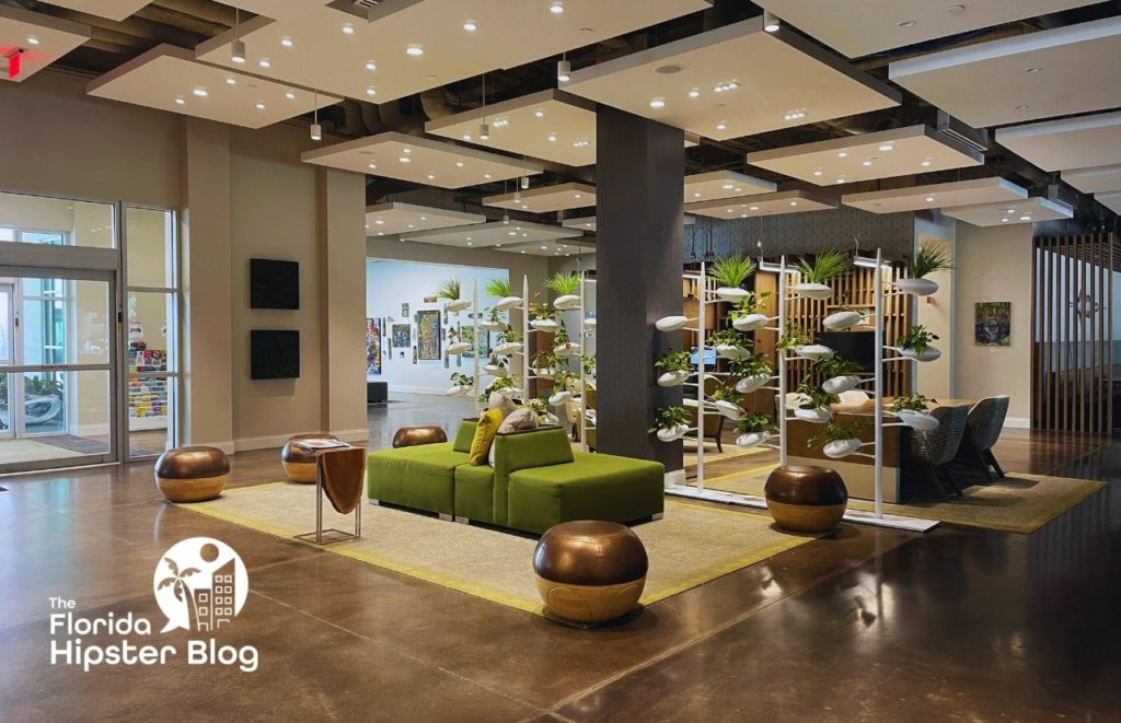 Hotel Indigo Gainesville Florida lobby area with green cushioned seating and lots of overhead lights and plants. Keep reading to learn more about Hotel Indigo Gainesville.