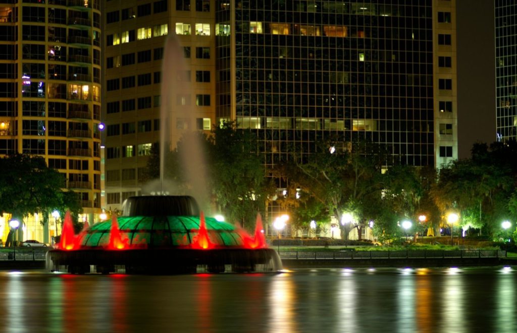 Lake Eola in Downtown Orlando with green and red water features for Christmas in Florida. Keep reading to discover more ideas for a couples night in Orlando.