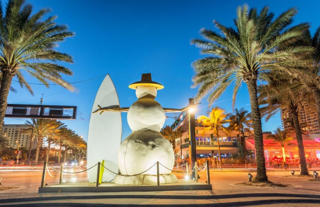 Snowman statue with surfboard amongst palm trees in Las Olas Fort Lauderdale Florida at Christmas. Keep reading to learn more about things to do in Florida at Christmas..