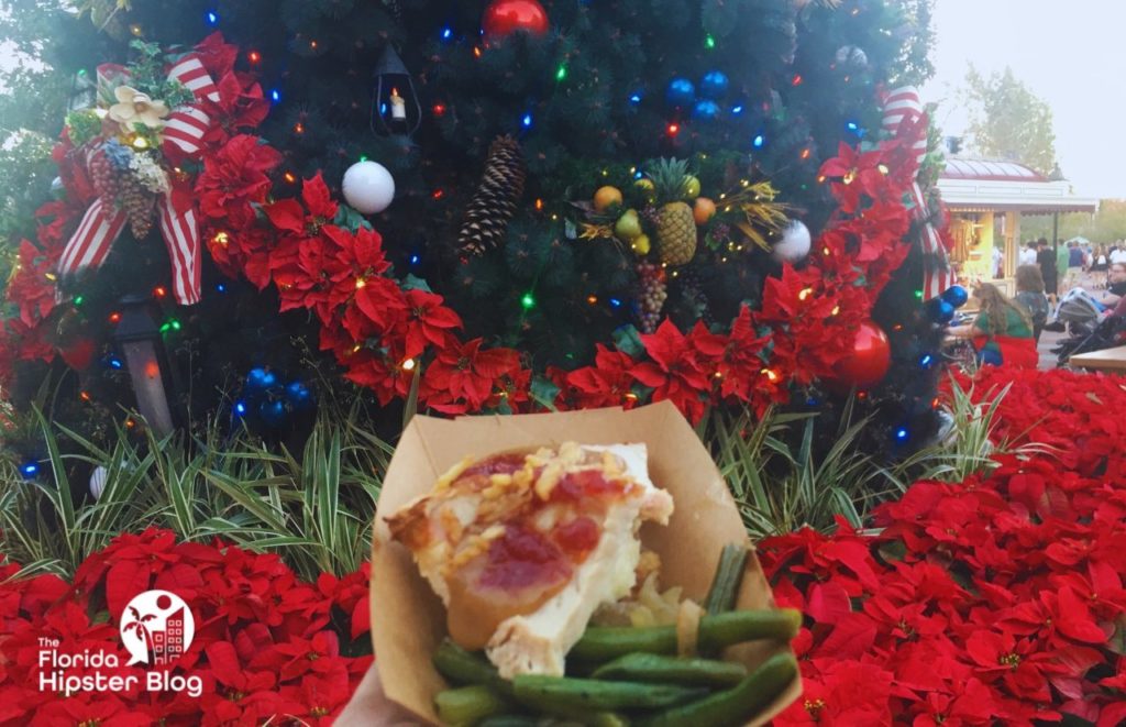 Epcot Festival of the Holidays with a food dish in front of the Christmas tree and poinsetta. Keep reading to discover the best things to do in Orlando for couples.