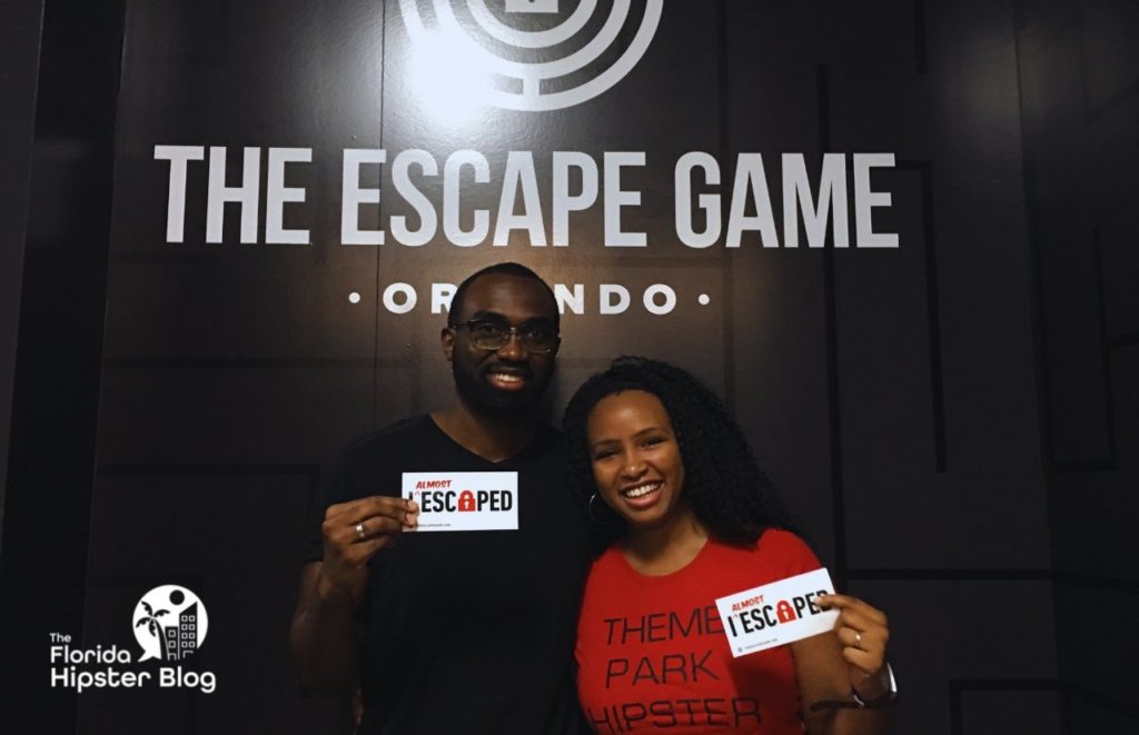 Escape Game Orlando with NikkyJ and her partner with an I almost escaped sign. Keep reading to discover more things to do for date night in Orlando.