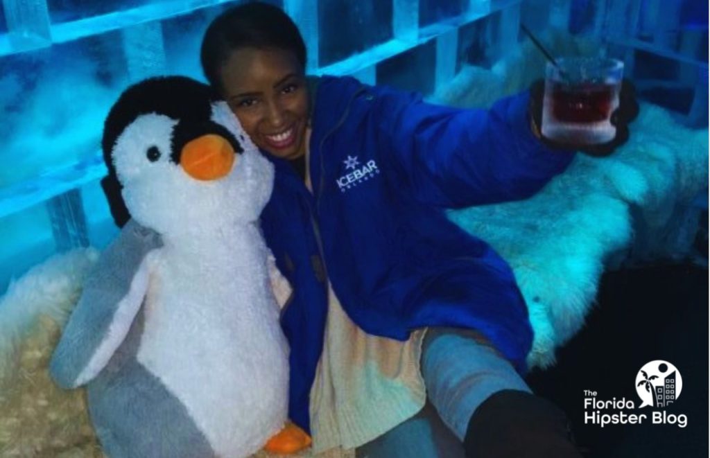 NikkyJ at ICE Bar with a drink and hugging a stuffed penguin. Keep reading to learn more about things to do in Orlando at night.