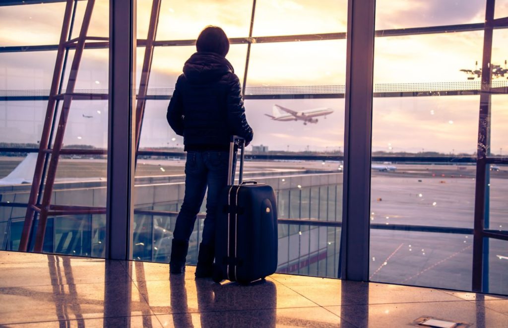 Lady standing front of airport window for JetBlue carry-on. Keep reading to learn more about flying JetBlue with a carry-on.