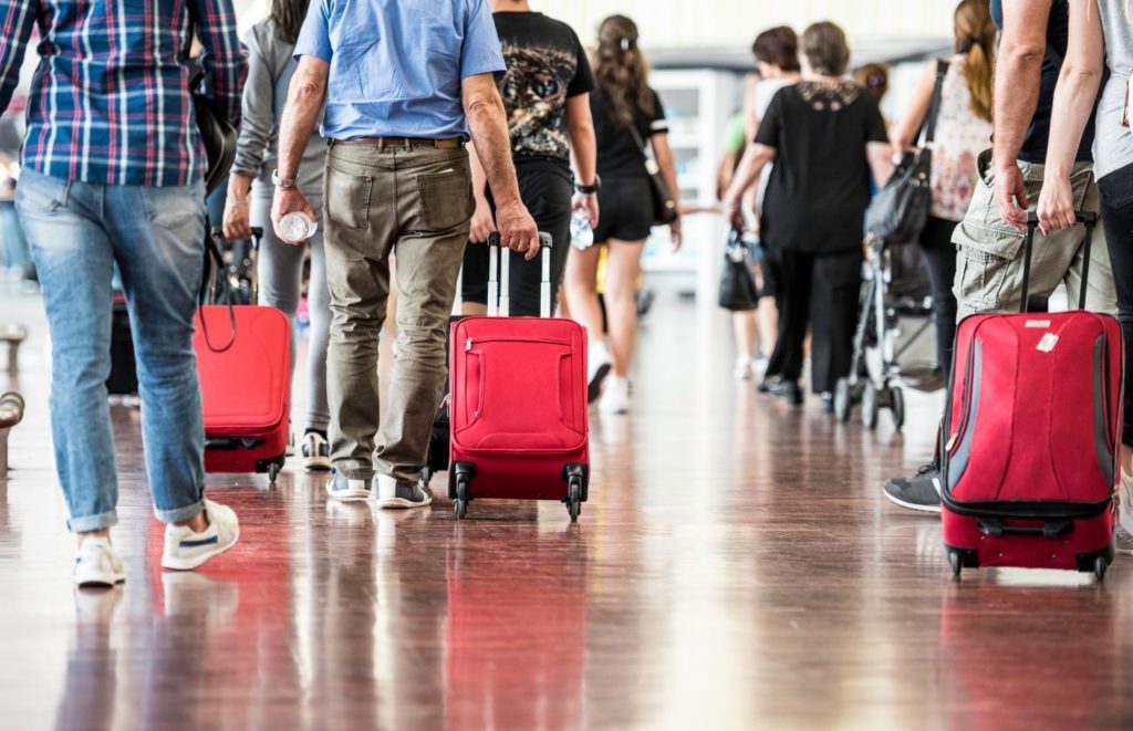 People walking in airport with luggage for JetBlue carry-on. Keep reading to find out all you need to know about JetBlue carry-on policy.