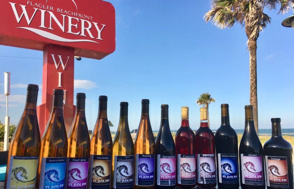 Wine bottles are lined up against the view of the beach from Flagler Beachfront Winery in Flagler Beach, Florida. Keep reading for more places to take a perfect day trip from Orlando, Florida. 