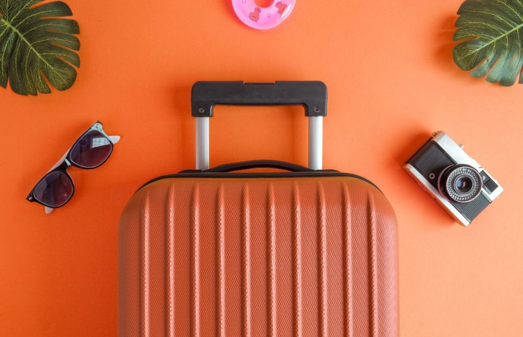 Orange suitcase next to sunglasses and camera. Keep reading to learn more about JetBlue carry-on policy.