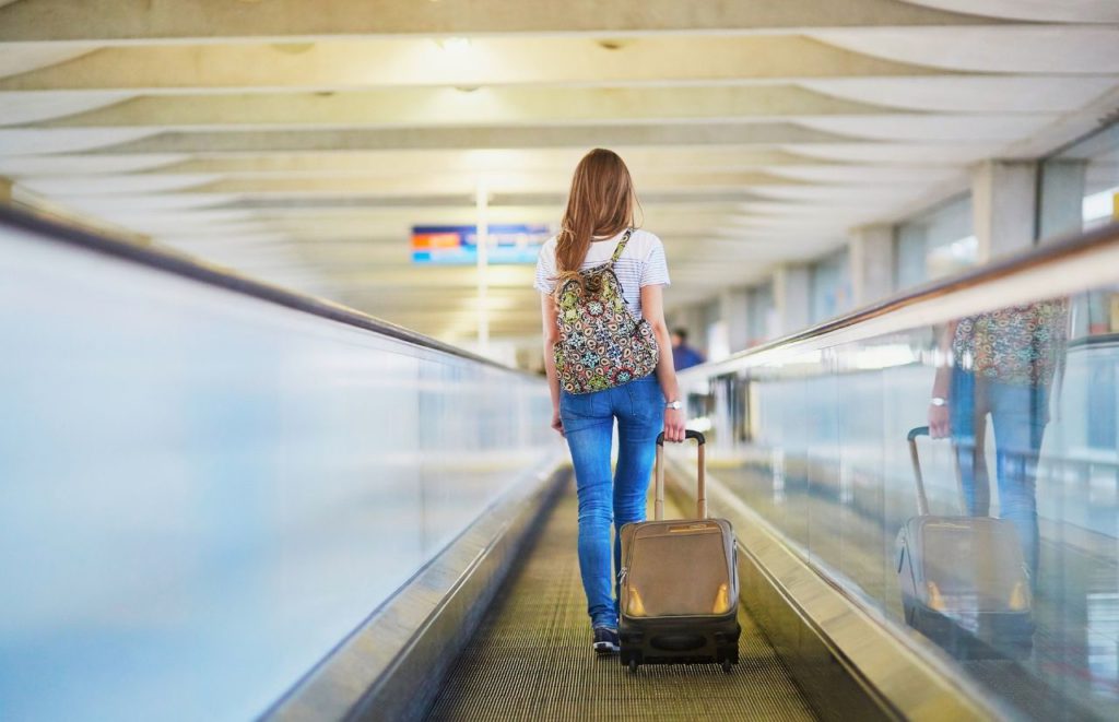 Can I Take a Backpack and a Carry-On with lady walking through airport. Keep reading to learn all you need to know about taking both a backpack and a carry-on on a plane. 