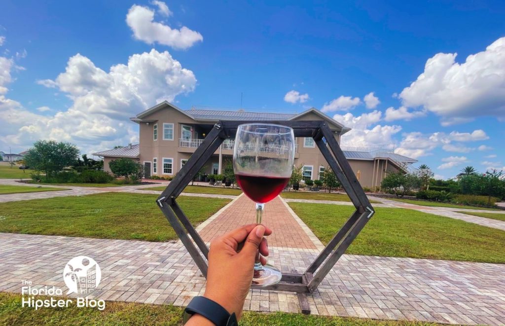 A glass of red wine is held up in front of Island Grove Wine Company at Formosa Gardens in Kissimmee, Florida. Keep reading for more places to get the best breakfast in Kissimmee, Florida. 