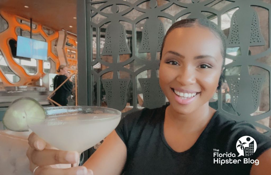NikkyJ holding a drink in a martini glass at the Dahlia Lounge  at Walt Disney World in Orlando, Florida. Keep reading for more romantic getaways in Orlando.