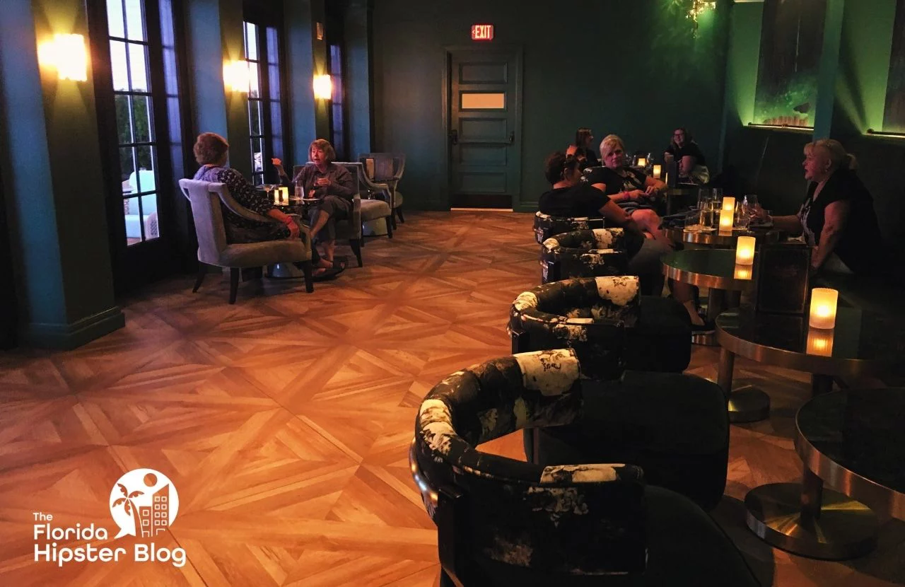 People sit at tables and round chairs on a wooden floor in at the Enchanted Rose Lounge at Disney's Grand Florida Resort & Spa in Orlando, Florida. Keep reading for more romantic getaways in Orlando.