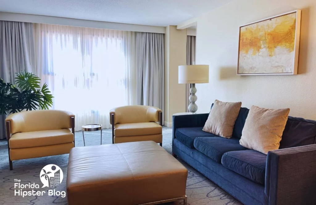 The interior of a suite at the Walt Disney Swan and Dolphin Resort in Orlando, Florida. There is a tan ottoman, blue couch, and two chairs. Keep reading for more options for where to stay in Orlando, Florida. 
