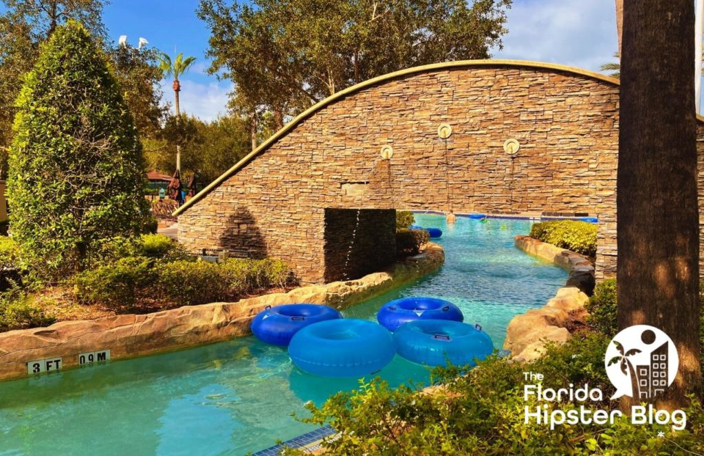 The lazy river at Signia By Hilton in Orlando Florida featuring lush greenery, blue inner tubes and a stone walkway. Keep reading for more options for where to stay in Orlando Florida. 