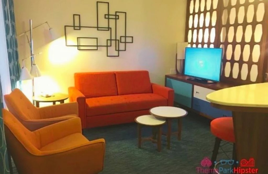 Interior view of a room at Universal Orlando Cabana Bay Beach Resort in Orlando, Florida shows a red couch, orange chairs and TV. Keep reading for more options for where to stay in Orlando, Florida.