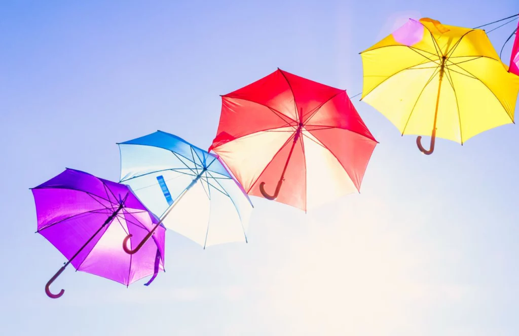 Colorful Umbrellas in the sunshine. Lady on Wooden Bridge in rain overlooking lake. Can I bring umbrella on plane? Keep reading to learn how.