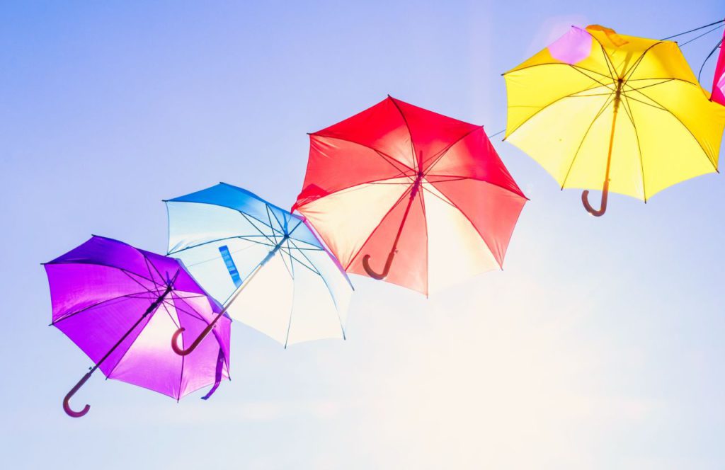 Colorful Umbrellas in the sunshine. Lady on Wooden Bridge in rain overlooking lake. Can I bring umbrella on plane? Keep reading to learn how.