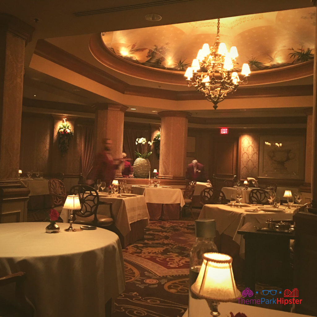 A chandelier and cloth-covered tables sit in a dimly lit room at Victoria and Albert's in Orlando, Florida. Keep reading for more on the best restaurants in Orlando, Florida. 