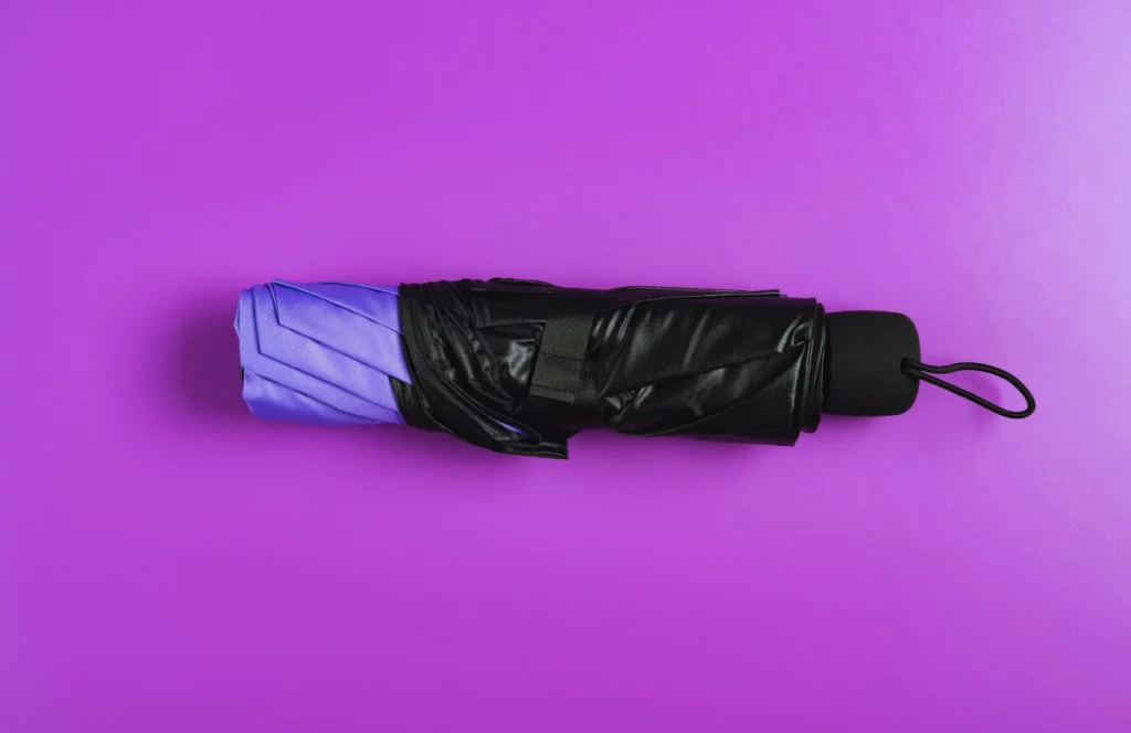 Foldable umbrella on purple background. Lady on Wooden Bridge in rain overlooking lake. Can I bring umbrella on plane? Keep reading to learn how.