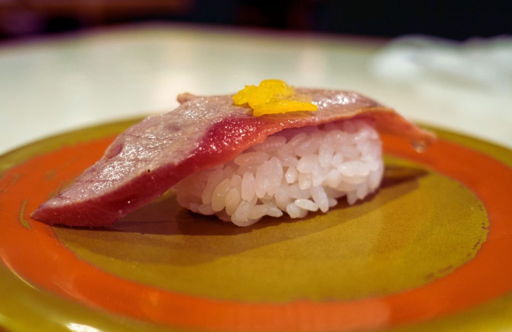 A piece of sushi sits on an orange and gold plate at Izakay Tori in Tampa, Florida. Keep reading for more places to get the best sushi in Tampa, Florida. 