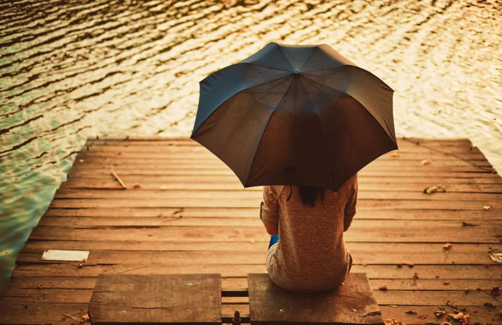 Lady on Wooden Bridge in rain overlooking lake. Can I bring umbrella on plane? Keep reading to learn how.
