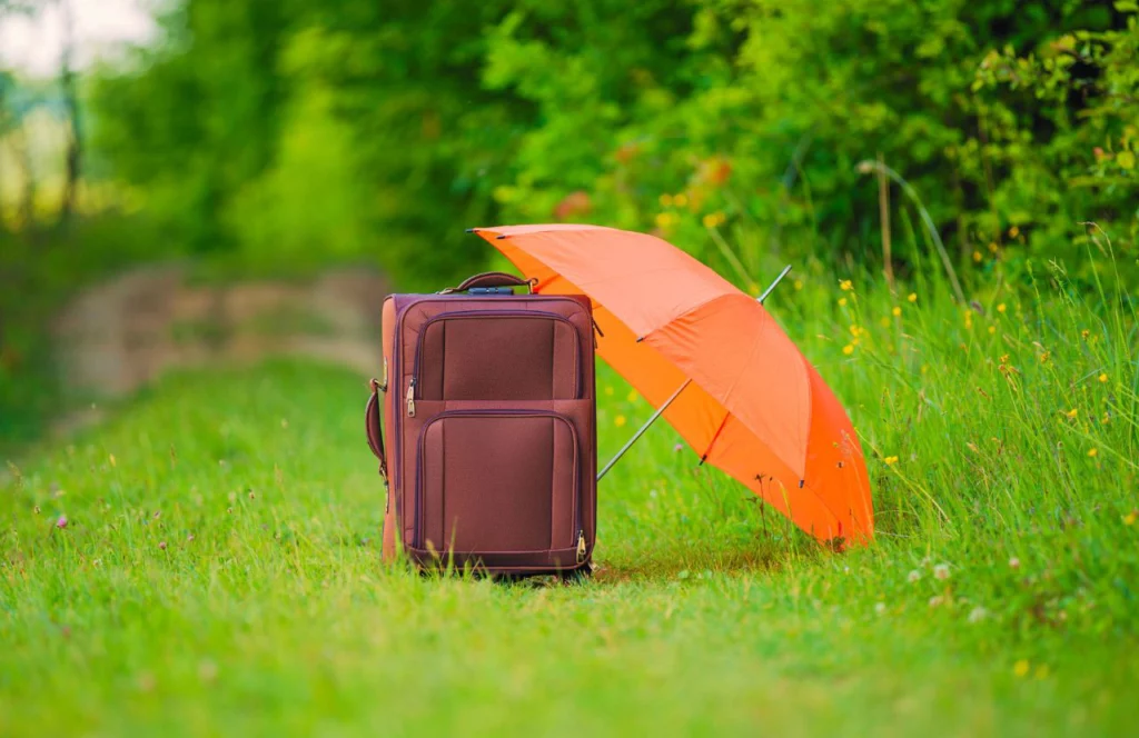 Orange umbrella next to black suitcase. Can I bring umbrella on plane? Keep reading to learn how.