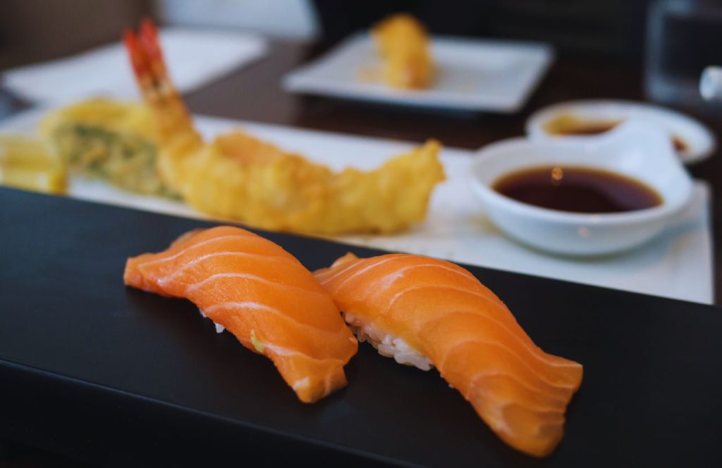 Umami Sushi in Tampa with sashimi on a dark place and tempura fried shrimp on another alongside soy dipping dishes. Keep reading to discover where to go for the best sushi in Tampa.  