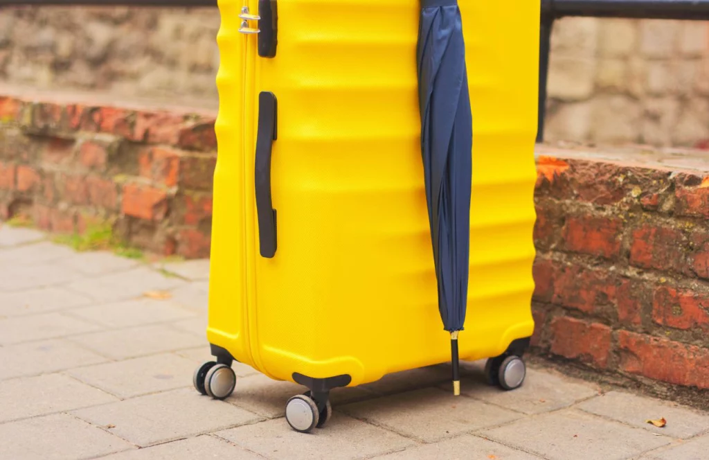 Yellow carry on suitcase with black full size umbrella. Can I bring umbrella on plane? Keep reading to learn how.