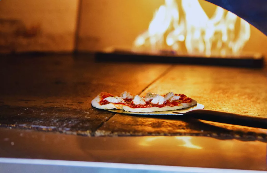 Fabrica Pizza one of the Best Pizza in Tampa showcasing an artisan pizza being put into the wood fire oven. Keep reading to find out the best pizza places in Tampa. 