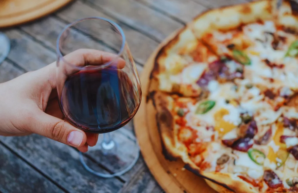 Wood Fired Pizza Wine Bar Best Pizza in Tampa with someone holding a glass of wine over a handcrafted pizza. Keep reading to find out all you need to know about the best pizza in Tampa. 