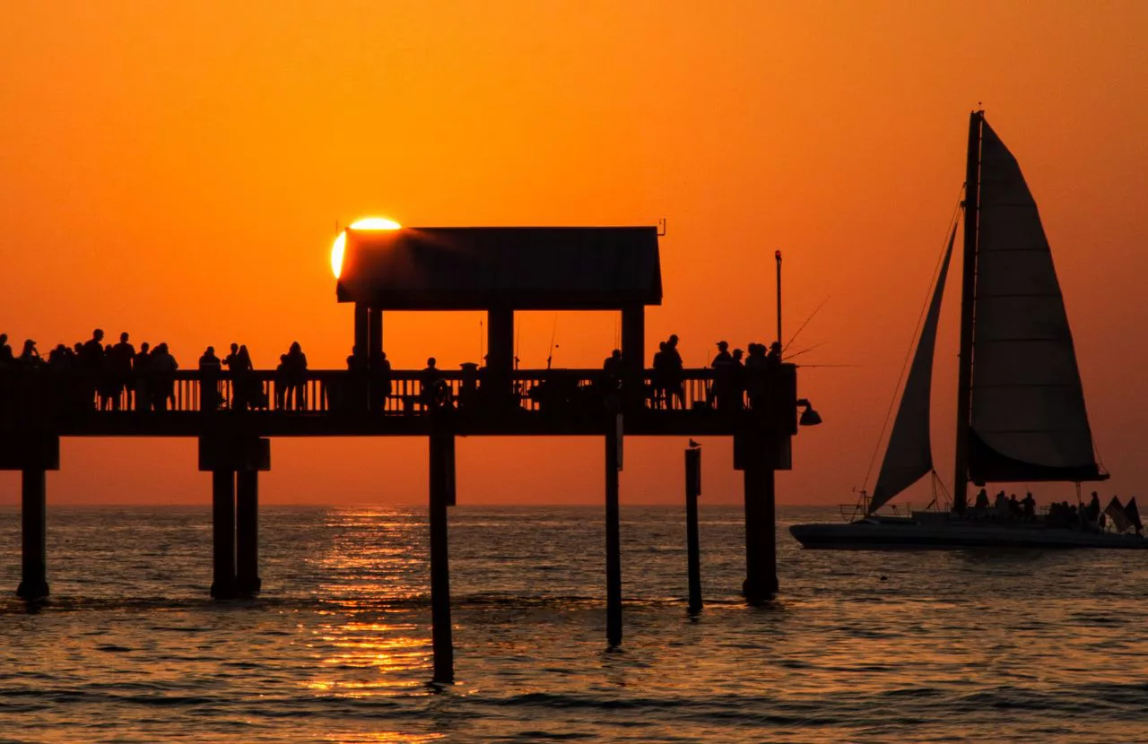 Clearwater orange sky at pier with sailboat. Keep reading to get the best places to watch sunset in Tampa, Florida