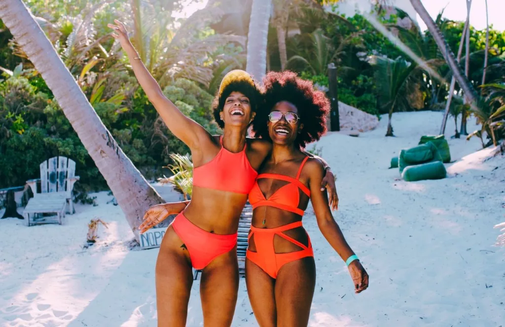 Girls Weekend on a Florida Beach black girlfriends enjoying each other on the beach with orange bikini bathing suits. Keep reading learn about what to pack for Florida and how to create the best Florida Packing List 