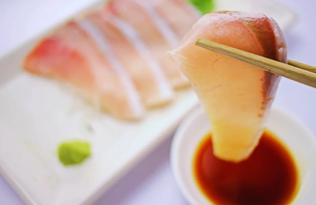 Yellowtail sashimi being held by chopsticks above a dish of soy sauce. Keep reading to get the full guide to Tampa sushi restaurants. 