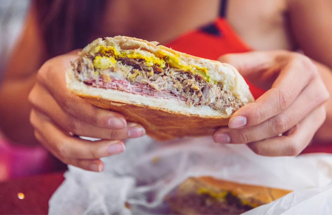 Keep reading to get the best breakfast in Tampa. Lady holding cuban sandwich in red dress at La Segunda Bakery and Cafe