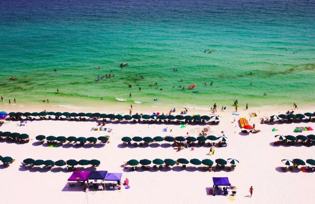 Crystal Sands Beach with beachgoers swimming gin the crystal-clear waters and beach umbrellas lined up down the beach. Keep reading to get the best beaches in Florida for bachelorette party.