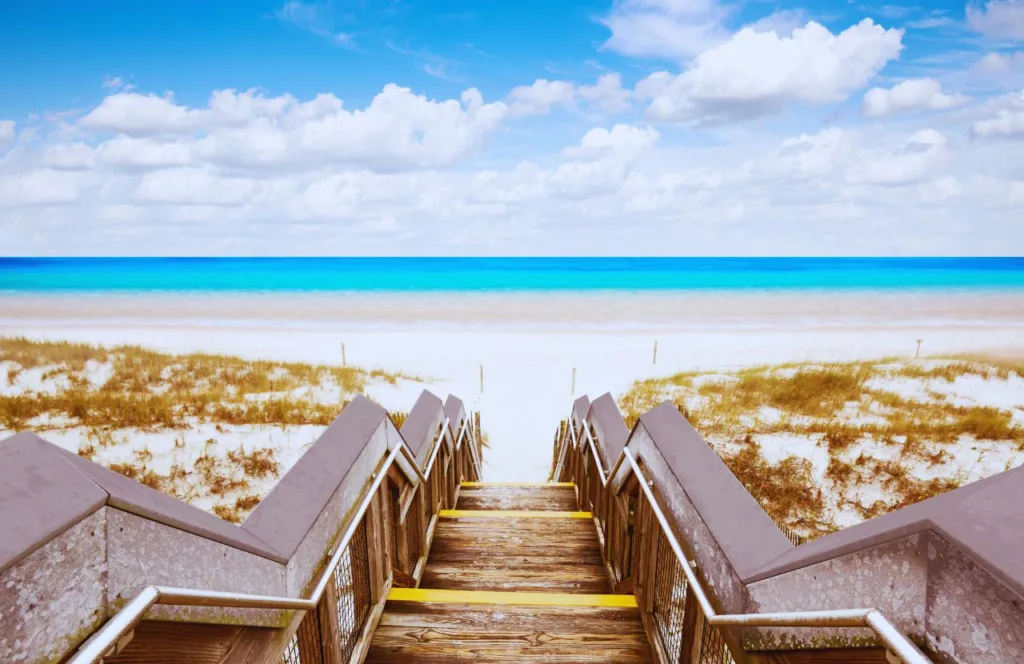 Henderson Beach State Park with bright blue clear water, sand dunes and a stair way down to the clean white sand. Keep reading to discover the best public beaches in Destin. 