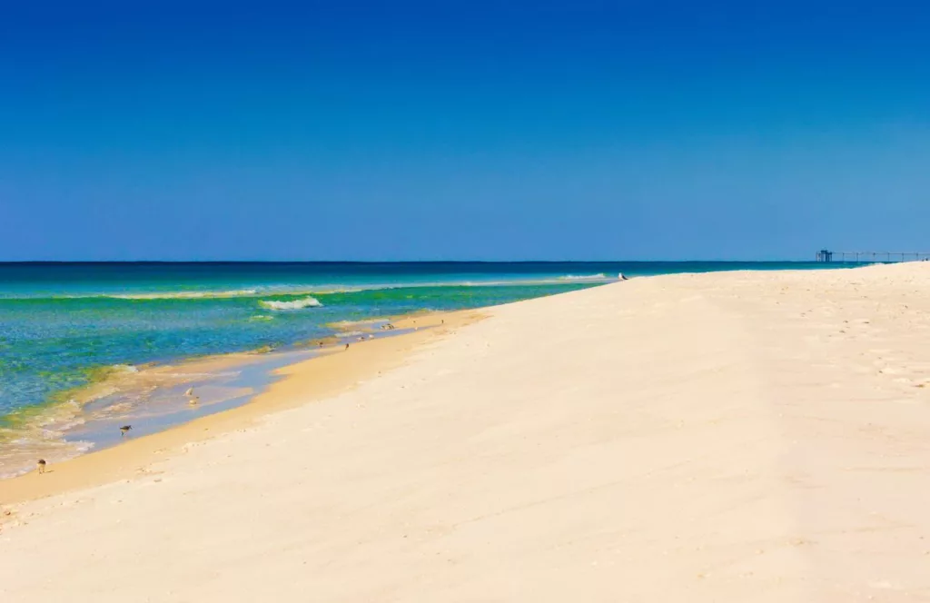 Destin, Florida sand dunes with emerald green and teal water with gentle waves. Keep reading to find out more about the best beaches in Destin Florida.