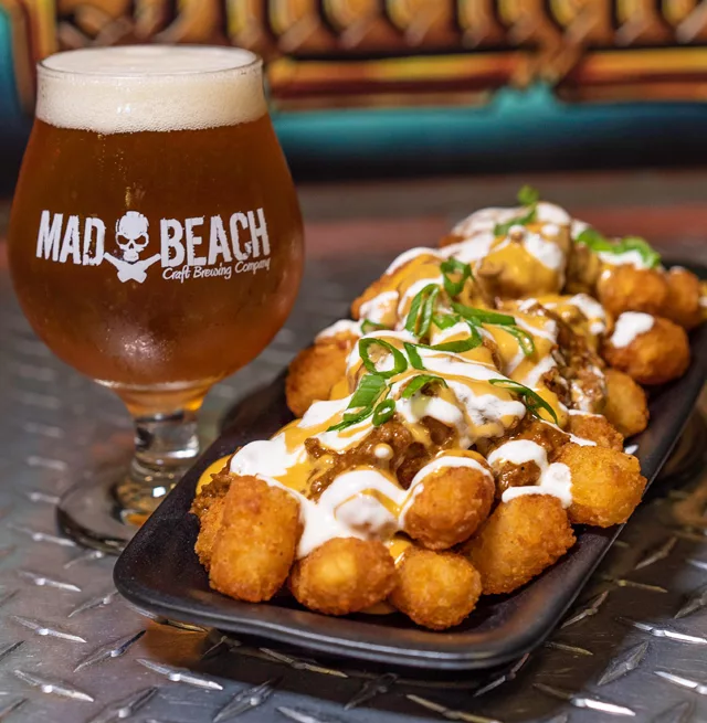 Mad Beach Craft Brewing Co. with beer next to loaded tater tots. Keep reading to discover the best bars in Treasure Island, Florida. 