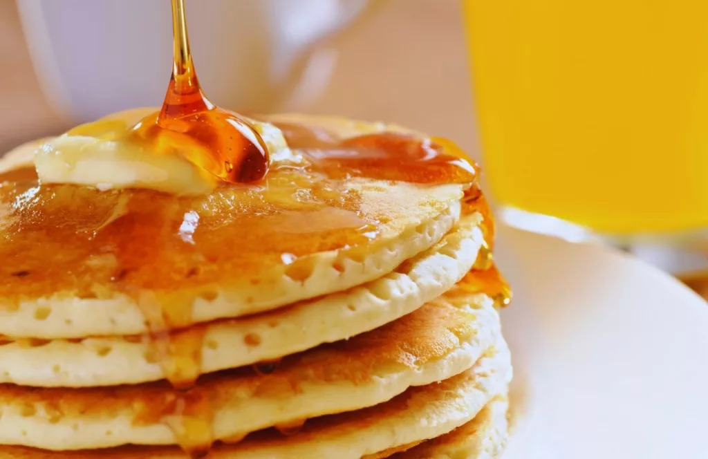 Pancakes topped with butter and syrup next to orange juice. Keep reading to find out where to eat in Naples. 