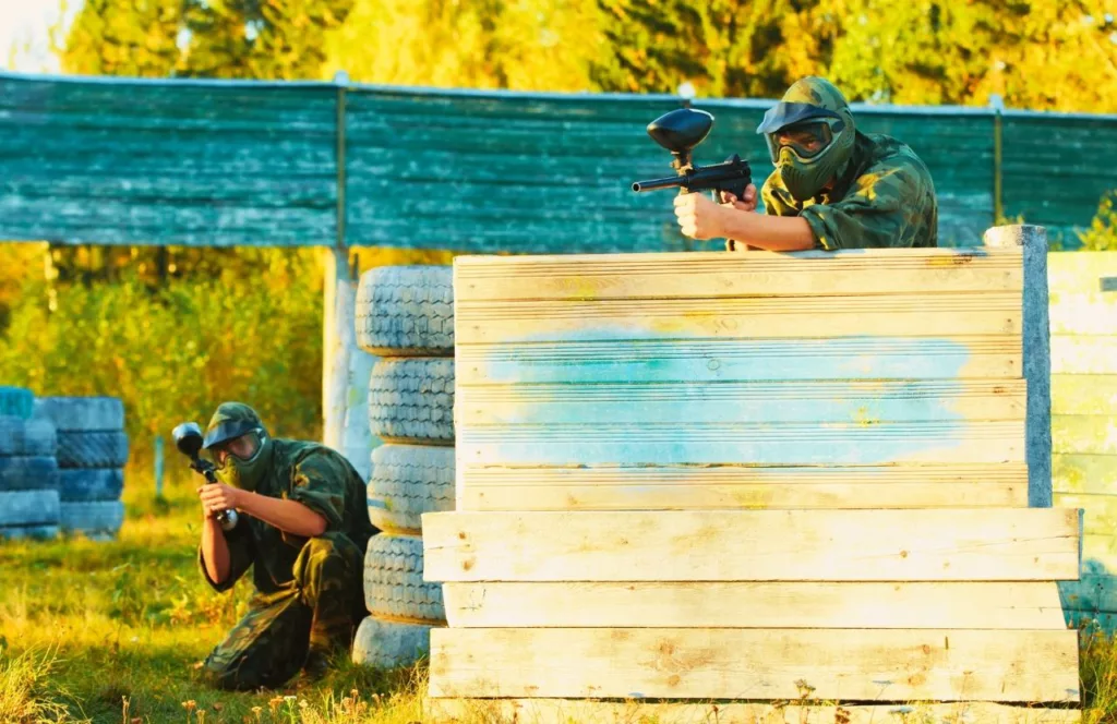 Men staying safe behind the stacks of wood and tires. Keep reading to get the Best Paintball Fields in Orlando, Florida.