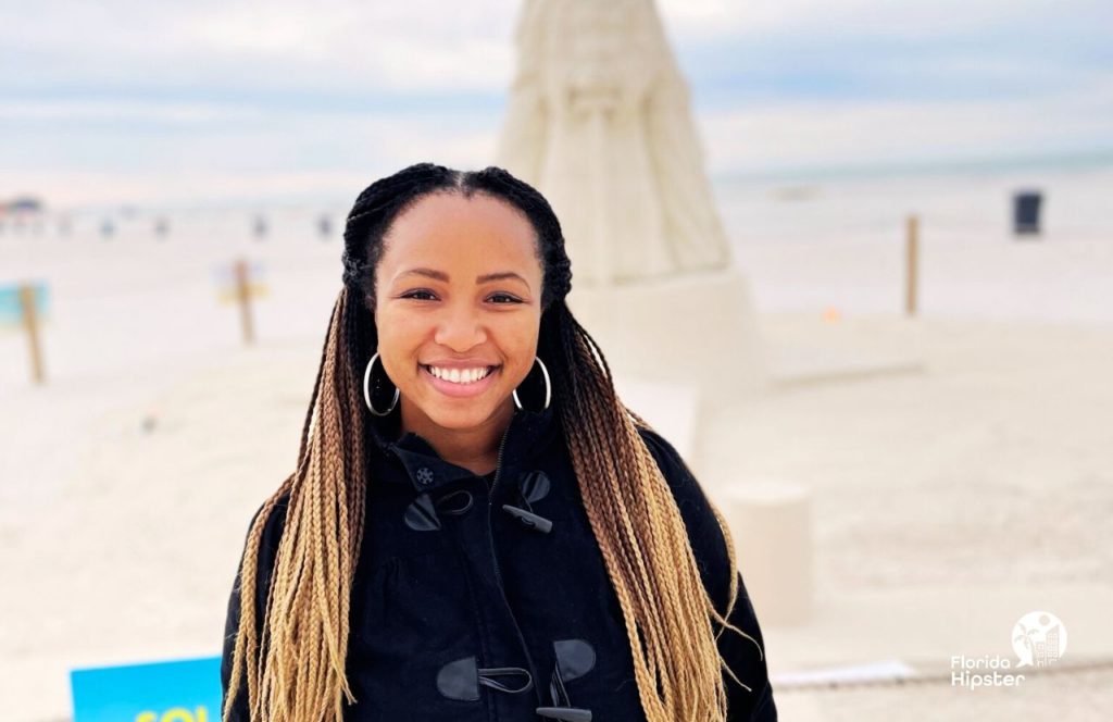 NikkyJ  in front of a sandcastle at a Florida sand sculpting competition. Keep reading to find out more about the best places to go on a beach vacation in Florida in November.